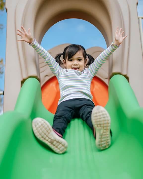 A little girl is sliding down a green slide.