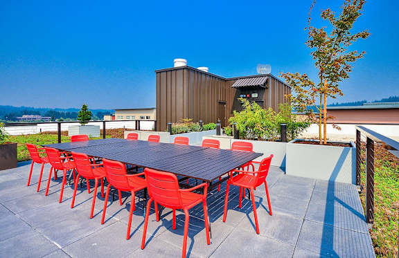 A table with red chairs is set up outside in front of a building.