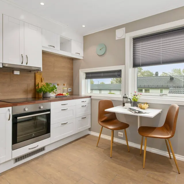 Modern kitchen with white cabinets, wooden countertops, an oven, and a small dining table with chairs by a window.