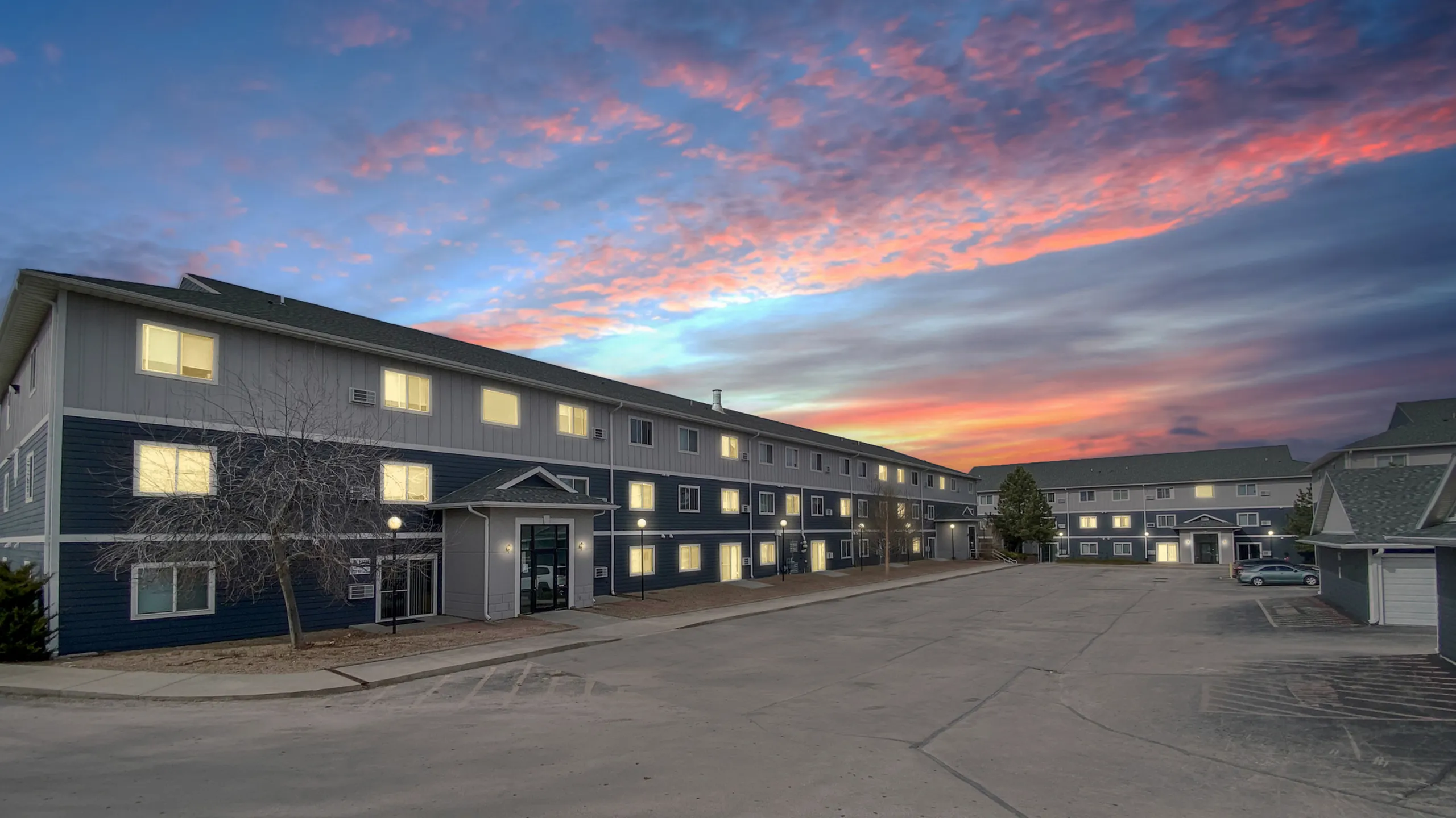 Charming three-story apartment complex at sunset with a vibrant sky, highlighting modern exterior design and warm, welcoming lights.