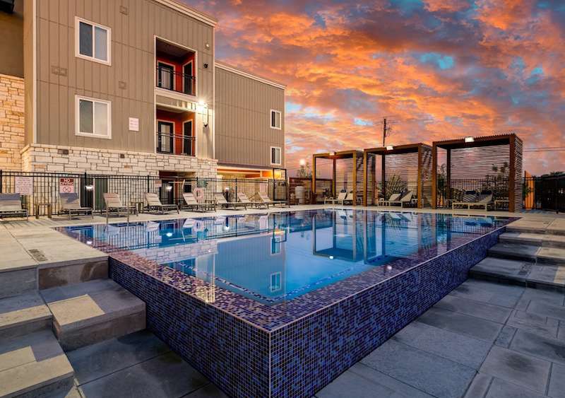 A swimming pool at The Oaks at Ben White with lounge chairs, and a sunset in the background.