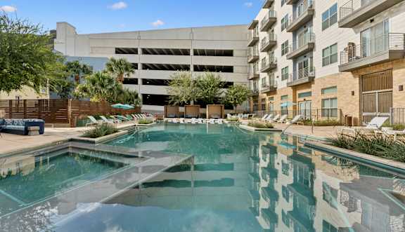 A swimming pool in front of a building with a parking garage.