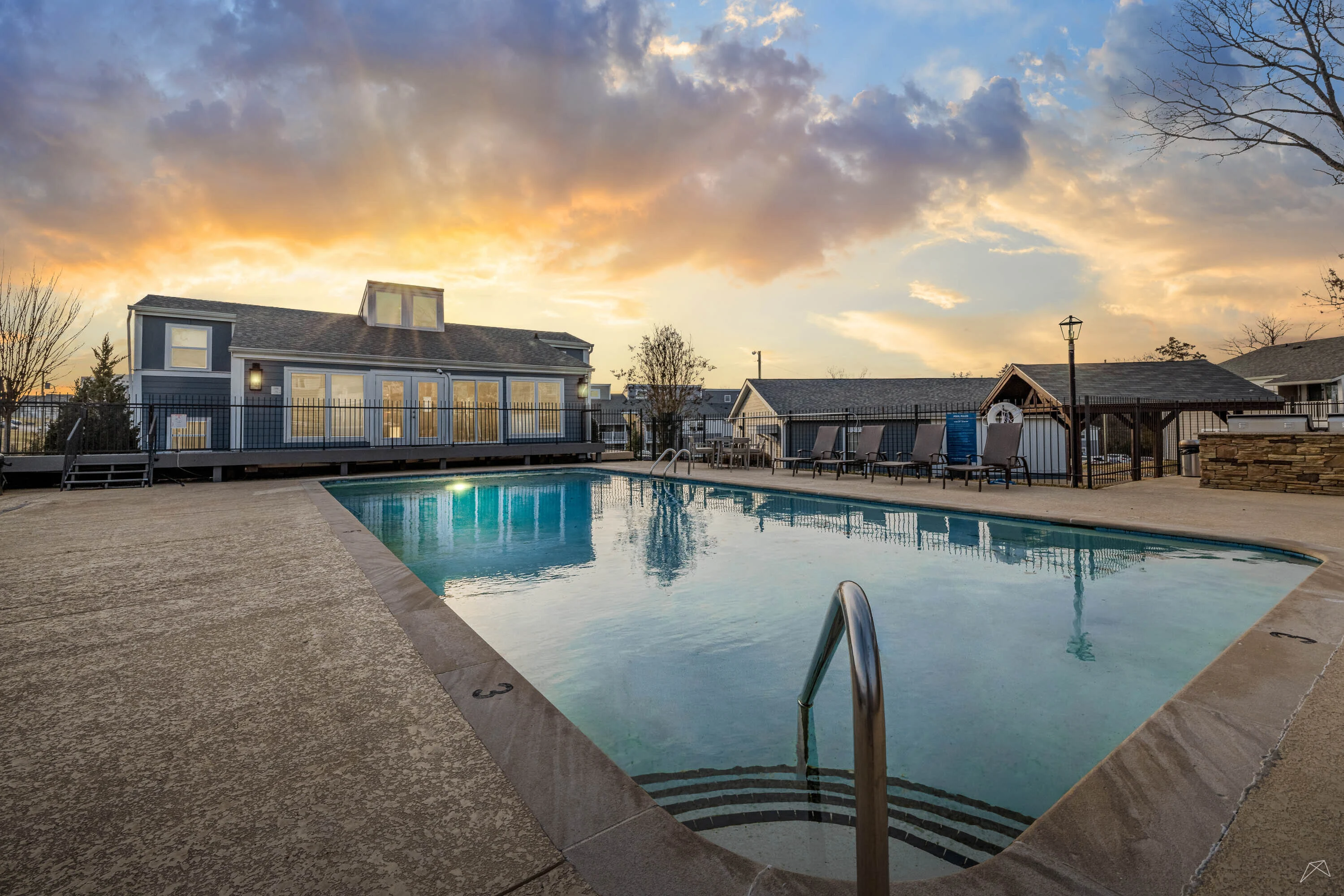 A serene apartment poolside scene with lounge chairs, a building in the background, and a sunset sky.