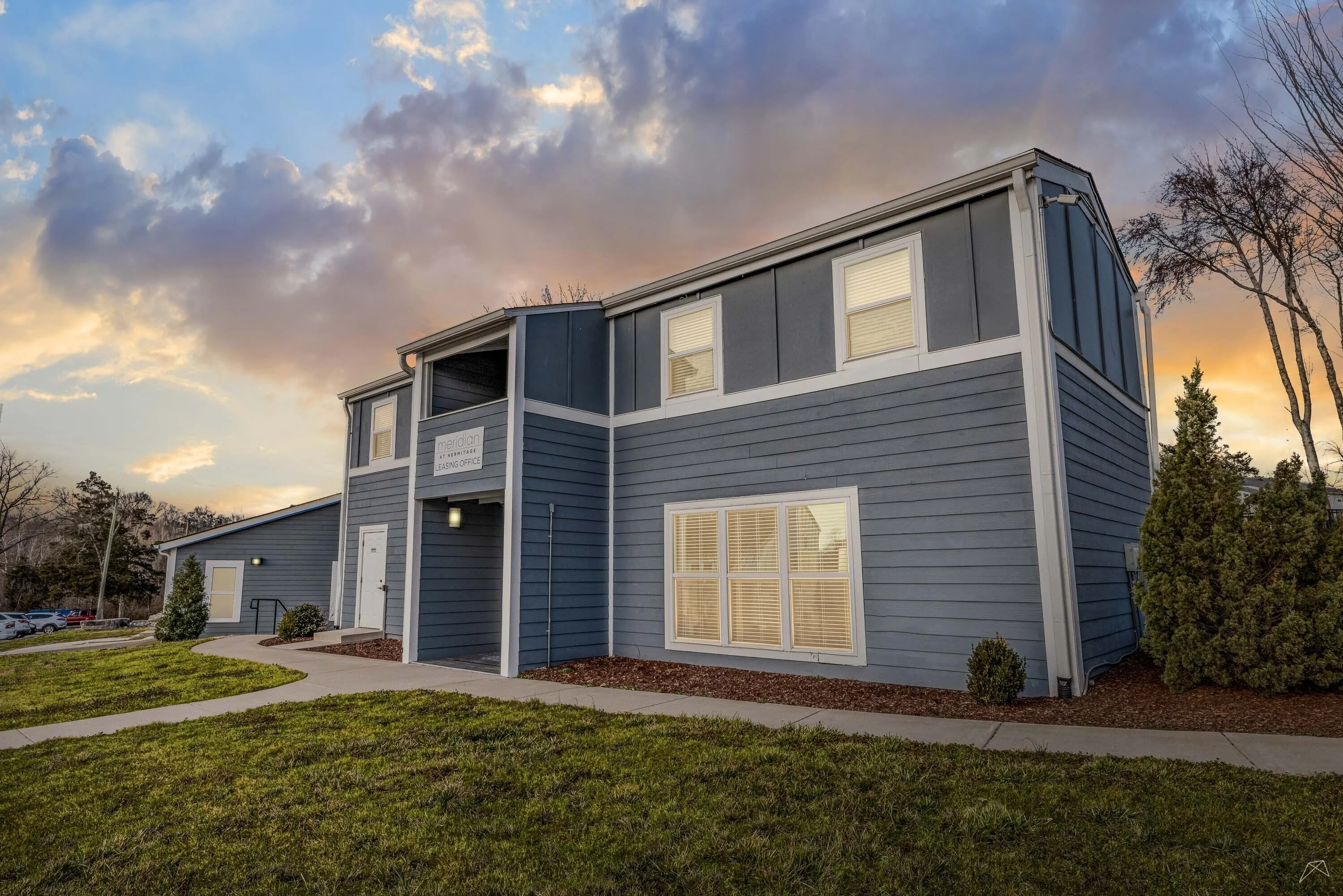 A blue apartment with a well-maintained exterior and landscaped grounds under a colorful sunset.