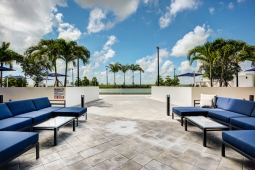 Two-Bedroom Apartments in Miami, FL - MB Station - An Outdoor Lounge with Lounge Seating, Glass Tables, Poolside Views, Surrounded by Trees and Raised Planters.
