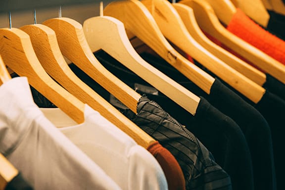 A row of wooden hangers with various shirts hanging on them.