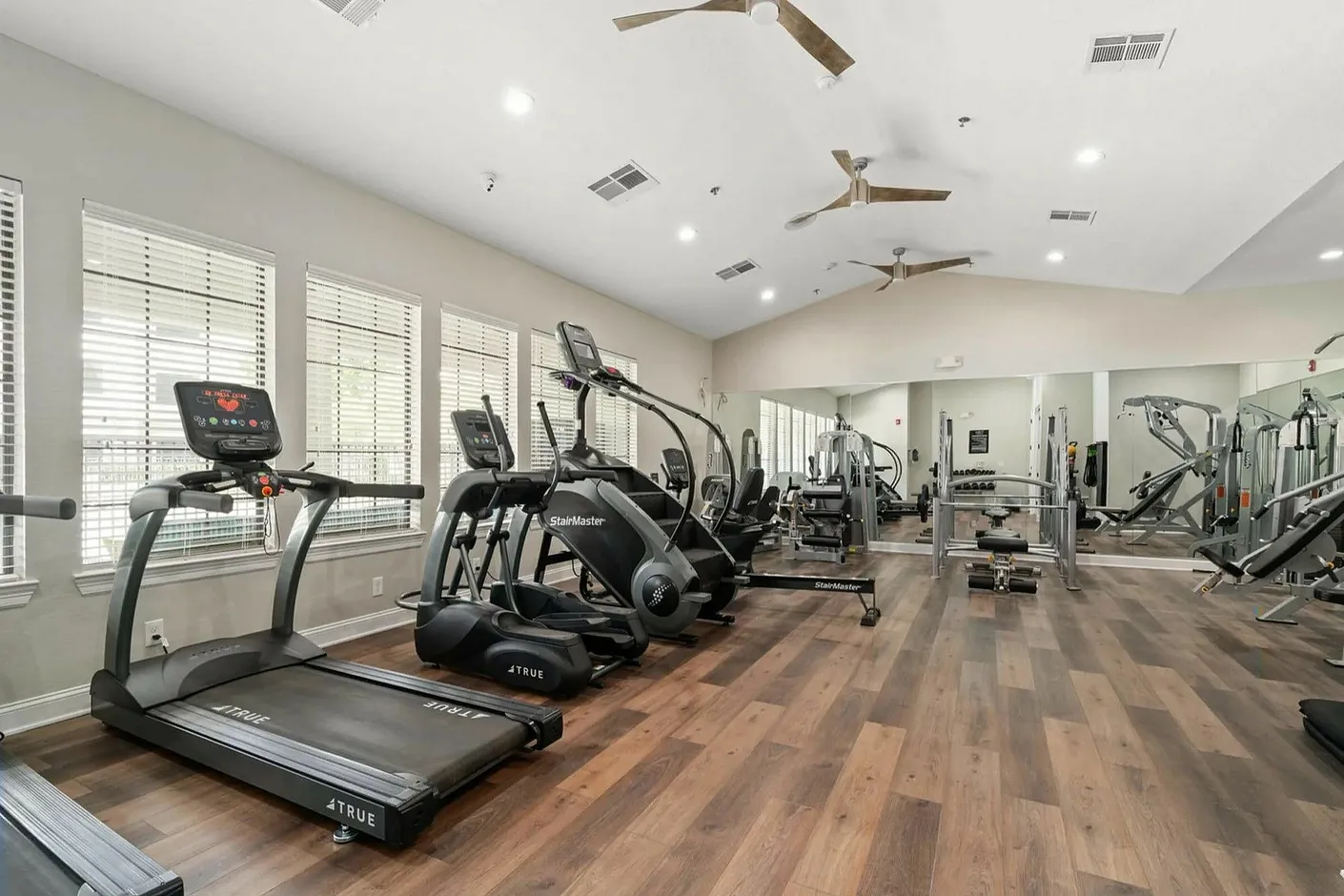 Modern apartment gym featuring state-of-the-art exercise equipment, sleek wood flooring, and abundant natural light.