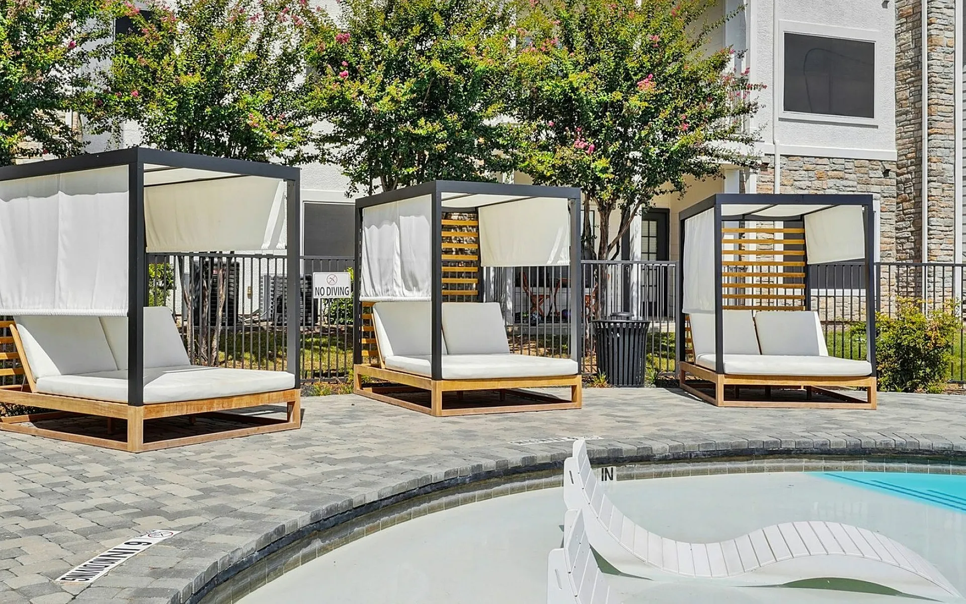 Inviting poolside cabanas with plush seating set against lush gardens, perfect for relaxation in a modern apartment setting.