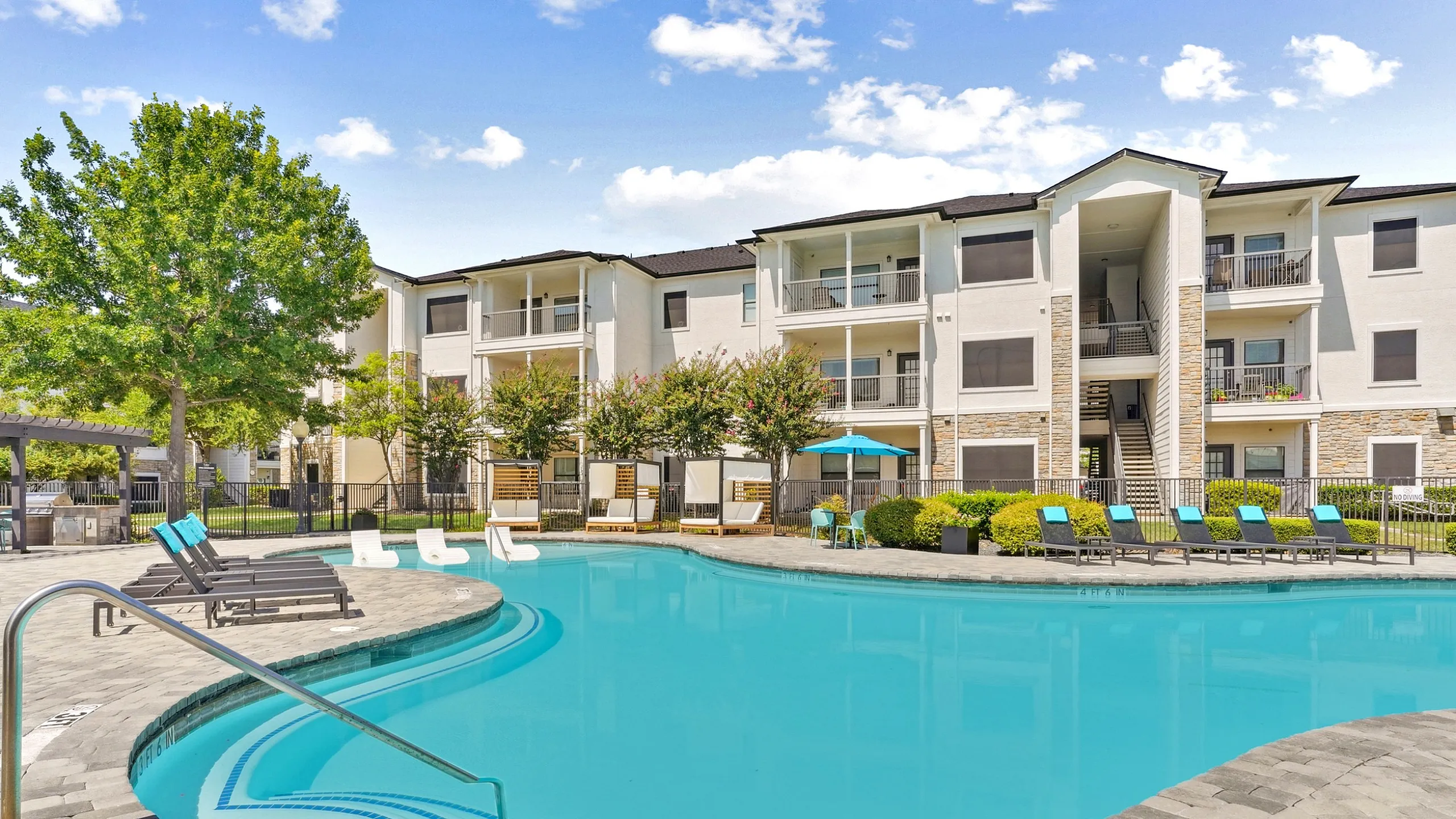 Luxurious apartment with a sparkling turquoise pool surrounded by stylish lounge chairs and vibrant greenery.