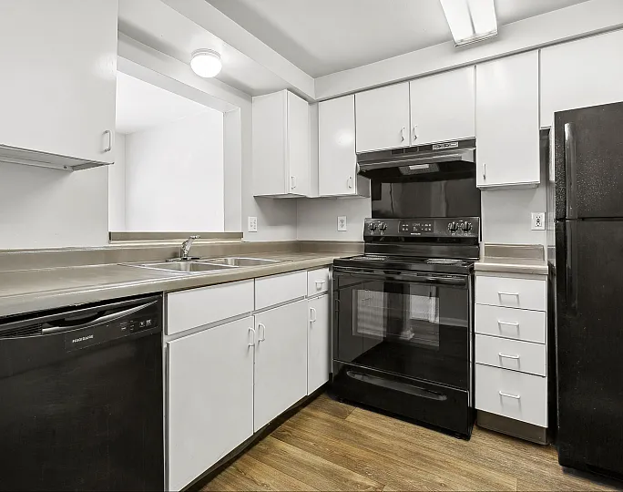 Modern kitchen with sleek white cabinets, black appliances, and elegant wood flooring.