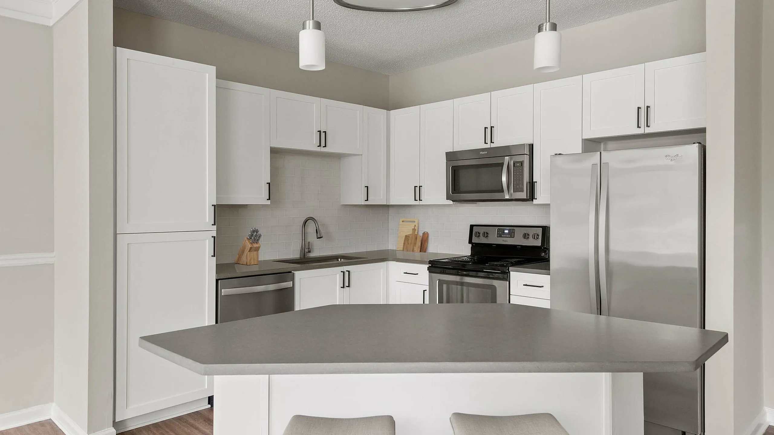 Sleek modern kitchen featuring a spacious island, white cabinetry, stainless steel appliances, and elegant pendant lighting.