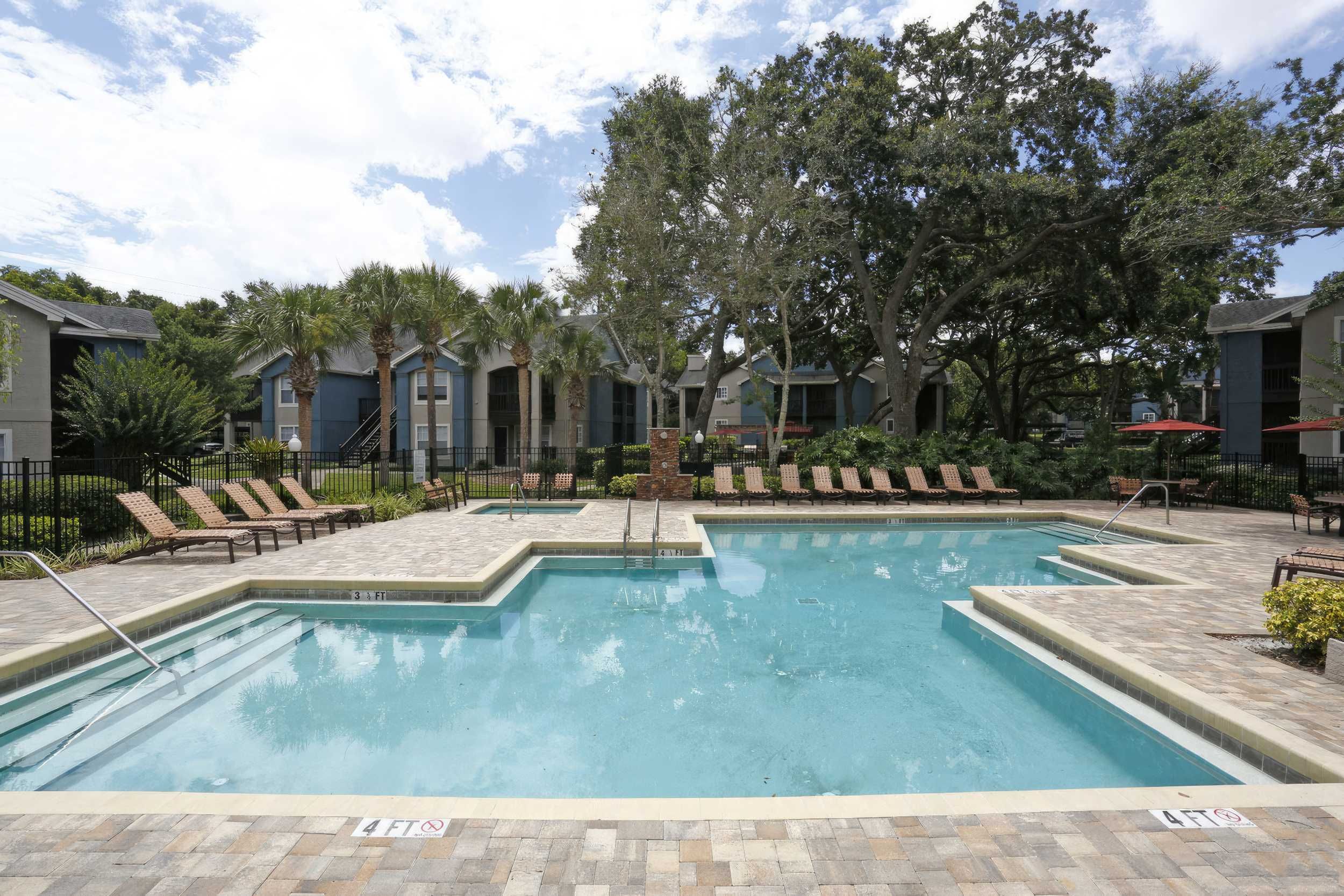 A serene apartment pool area with lounge chairs, surrounded by greenery and buildings.