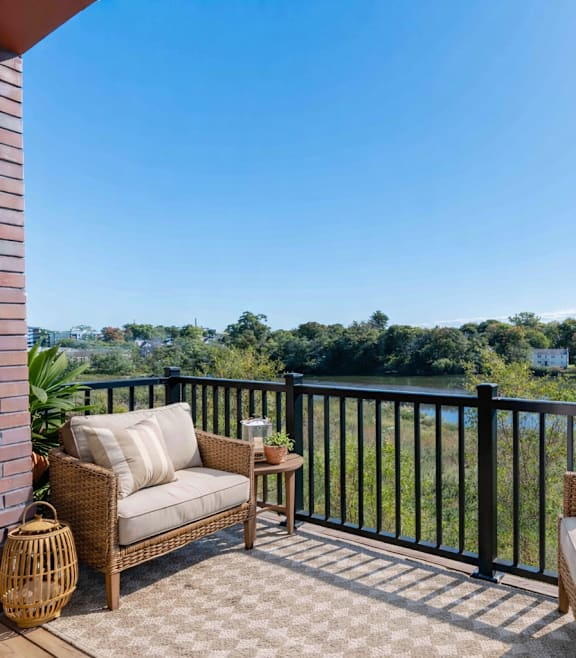 A balcony with a black railing overlooks a body of water and greenery.