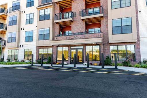Front entrance of Creekline at Fairfield apartments in Fairfield, CT featuring a modern brick-and-siding exterior, glass entry doors, and balcony residences above.