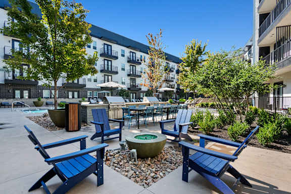 A sunny day at a courtyard with blue chairs and a fire pit at Abstract at Design District in Dallas, TX