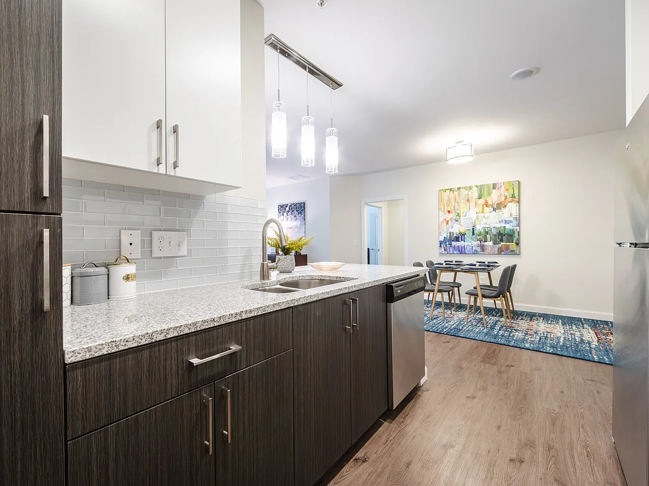 Modern kitchen with sleek wood cabinetry, granite countertops, and stainless steel appliances leading to a cozy dining area with contemporary art.