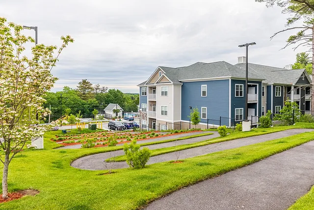 Charming apartment complex with elegant blue siding, surrounded by lush green landscaping and walking paths.