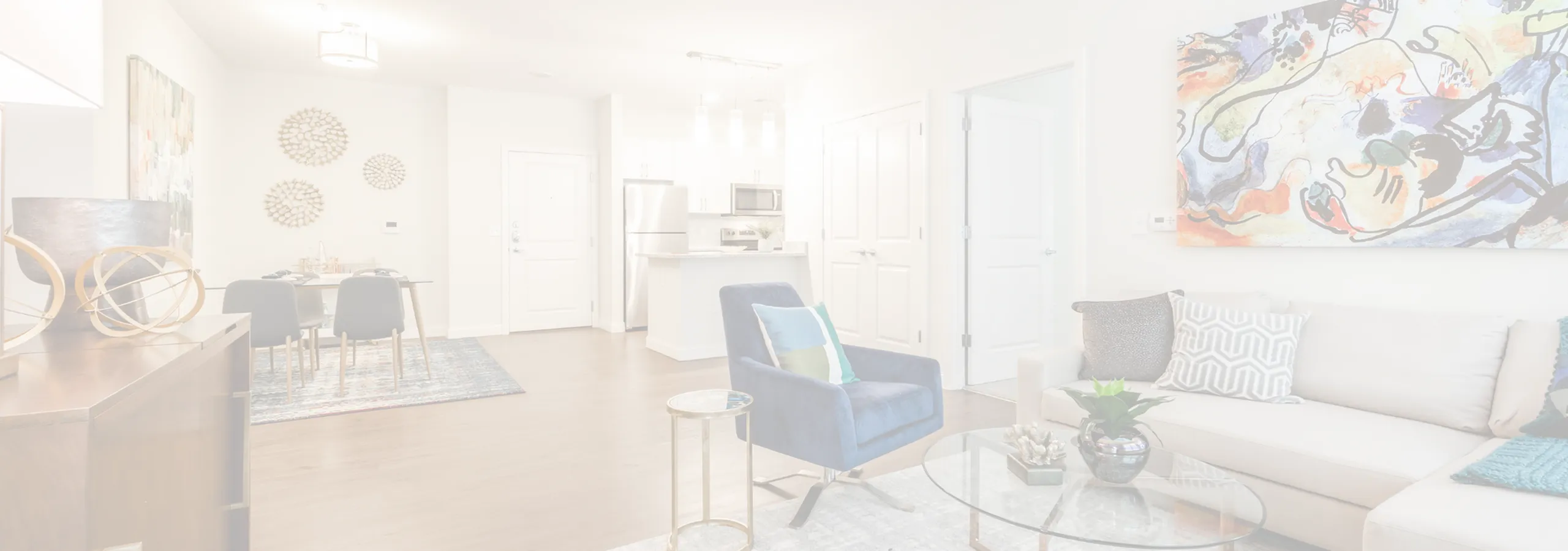 Modern open-concept living room with stylish décor, featuring a vibrant abstract painting, plush seating, and a sleek kitchen in the background.