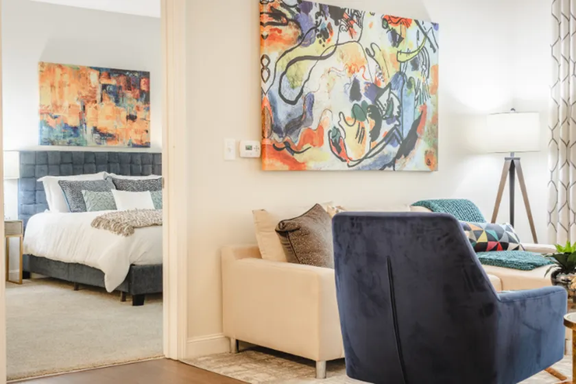 Inviting living room with modern artwork and cozy seating, seamlessly connecting to a stylish bedroom with a plush bed and vibrant decor.