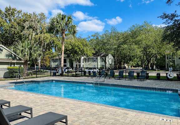 A swimming pool surrounded by trees and chairs.
