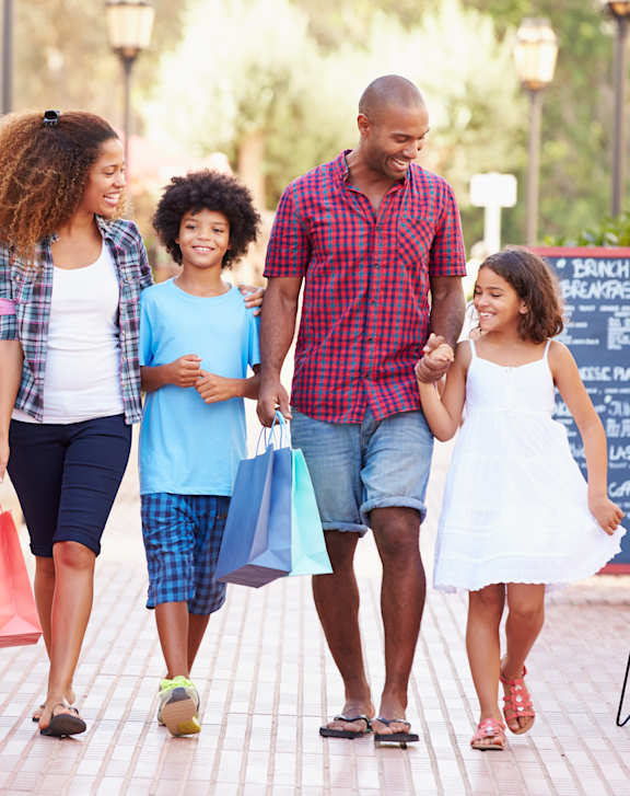 A family of four walking down a sidewalk holding hands.