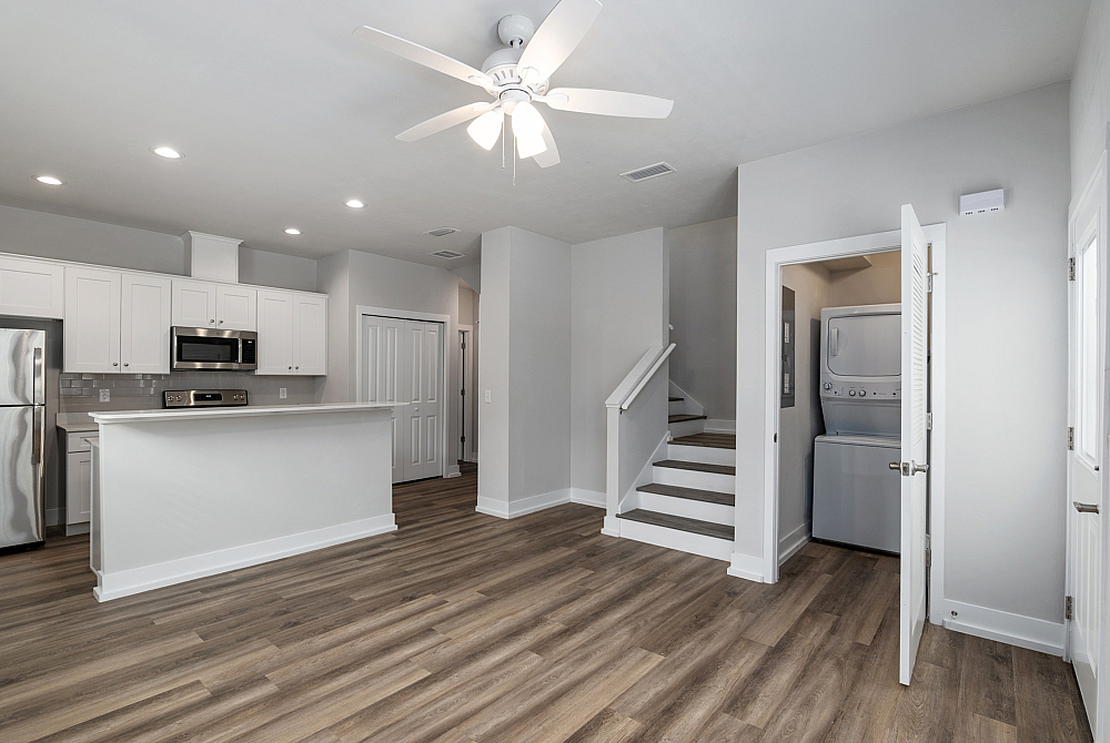 Modern open-concept living space with sleek kitchen and stainless steel appliances, elegant wood flooring, and convenient in-unit laundry room.