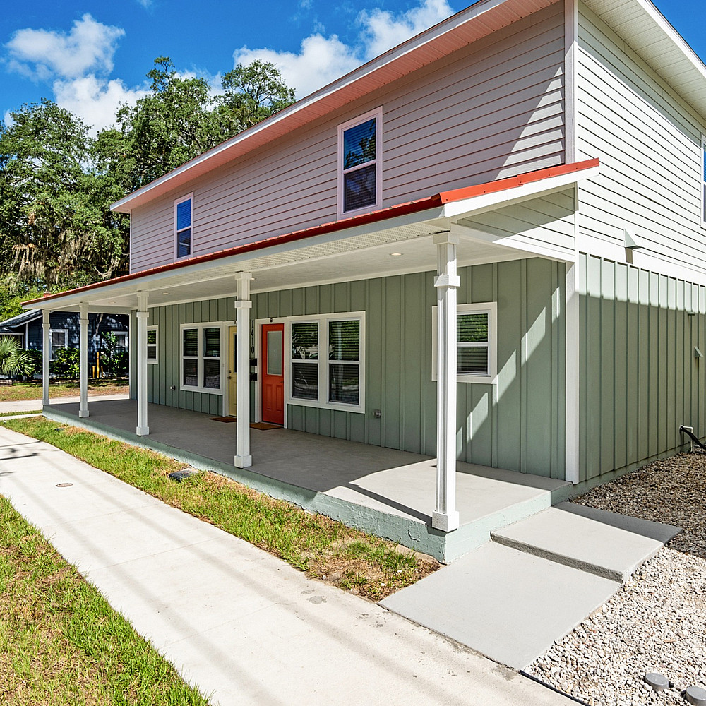 Charming two-story house with a welcoming front porch, set against a backdrop of lush greenery and clear blue skies.