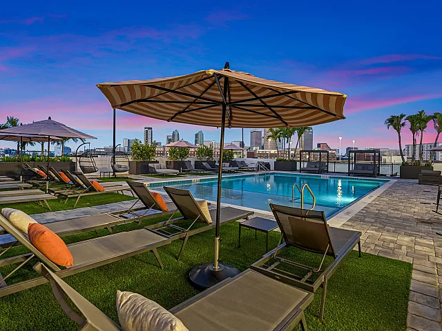 Luxurious rooftop pool area with stylish lounge chairs, vibrant umbrellas, and breathtaking city skyline views at sunset.