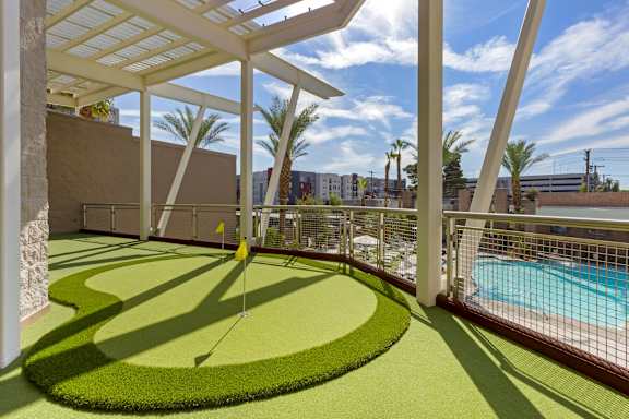A golf putting green is surrounded by a pool and palm trees.