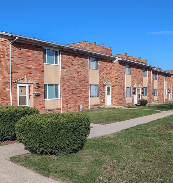 A row of red brick houses with green bushes in front.