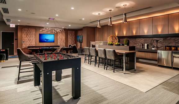 A modern room with a foosball table, bar, and television.