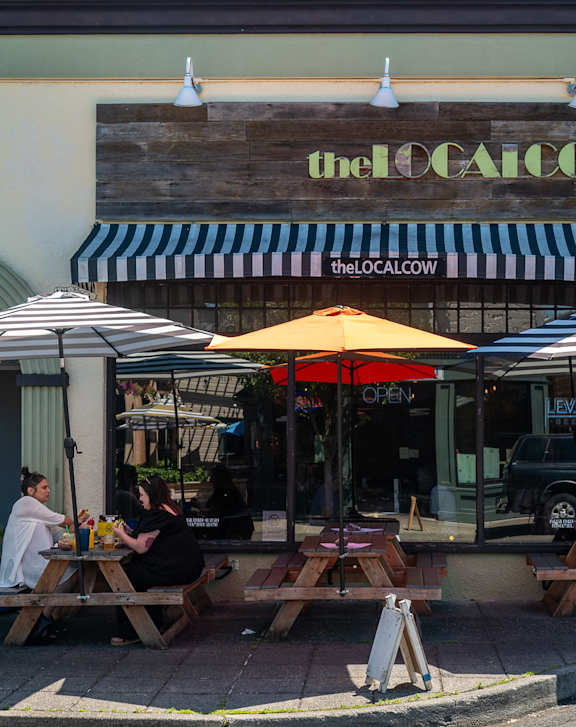 A restaurant named "the local cow" has tables and chairs outside.