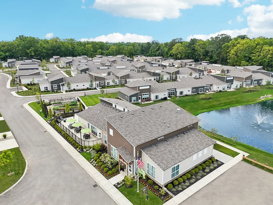Charming aerial view of a vibrant community featuring modern single-story homes, a scenic pond with a fountain, lush greenery, and inviting outdoor seating areas.