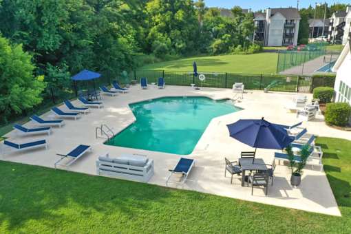 A large outdoor swimming pool surrounded by lawn chairs and umbrellas.