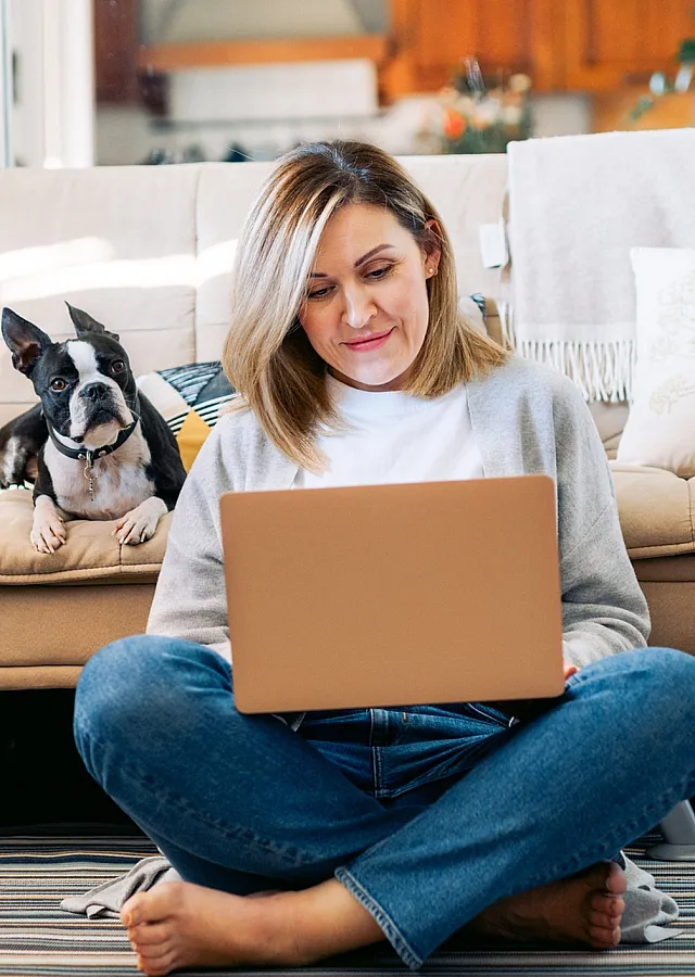 Cozy living space with a woman working on a laptop, accompanied by her dog on a comfortable sofa, exuding warmth and tranquility.