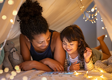 Cozy apartment setting with a joyful mother and child under a blanket fort, illuminated by charming string lights, fostering a warm and inviting ambiance.
