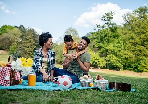 Joyful family enjoying a lively picnic on a sunny day in a beautiful park, complete with a picnic basket, flowers, and a soccer ball.