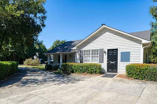 A house with a grey siding and a black door is surrounded by green bushes.