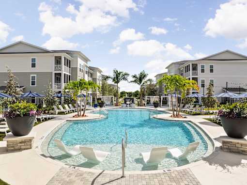 A swimming pool surrounded by white chairs and potted plants at Verity Luxury Apartments, Vero Beach