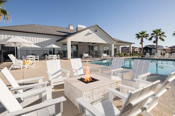 A poolside patio with white chairs and a fire pit.