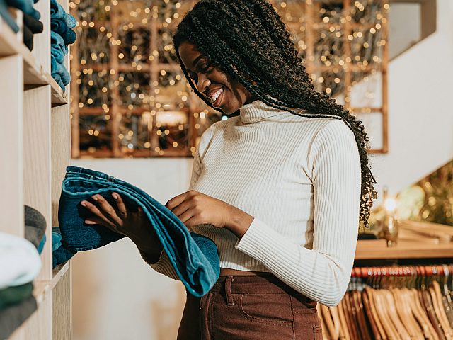 Stylish boutique scene with a smiling person organizing denim jeans under warm, festive lighting.