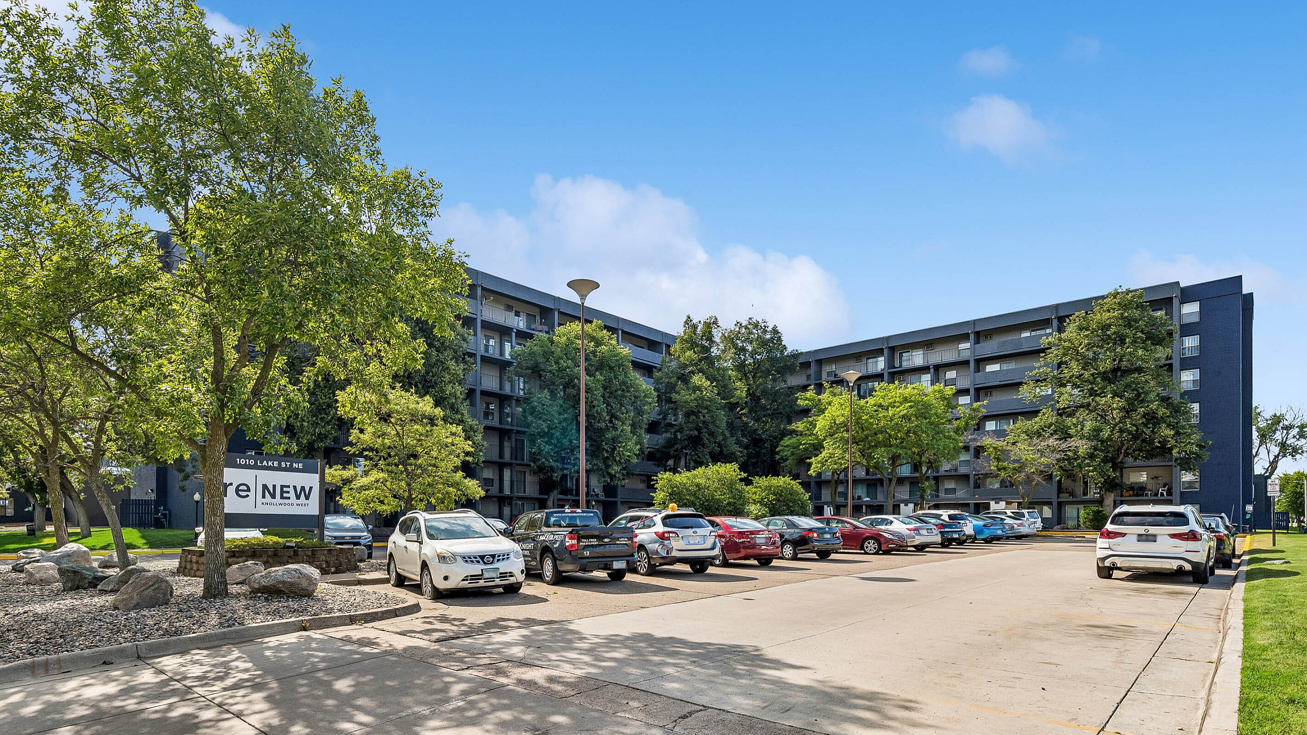 Contemporary apartment complex with lush greenery and ample parking on a sunny day, highlighting modern urban living.