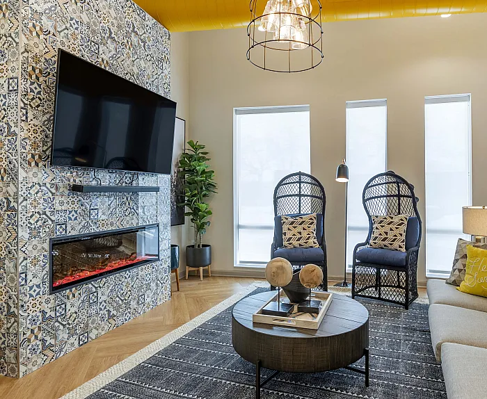 Chic living room with patterned tile fireplace, large TV, and modern decor. Cozy seating with stylish chairs and a plush sofa accented by colorful cushions. Bright and inviting ambiance with a contemporary touch.