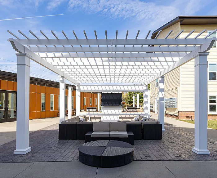 Chic outdoor lounge under a stylish white pergola, surrounded by vibrant architecture, perfect for relaxing afternoons.