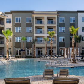 Dog-Friendly Luxury Apartments in Savannah, GA - Aventon Victory - Resort-Style Pool with Saltwater, with Sun Shelf, Umbrellas with Table and Chairs Surrounded by Tanning Lounge Chairs with Palm Trees