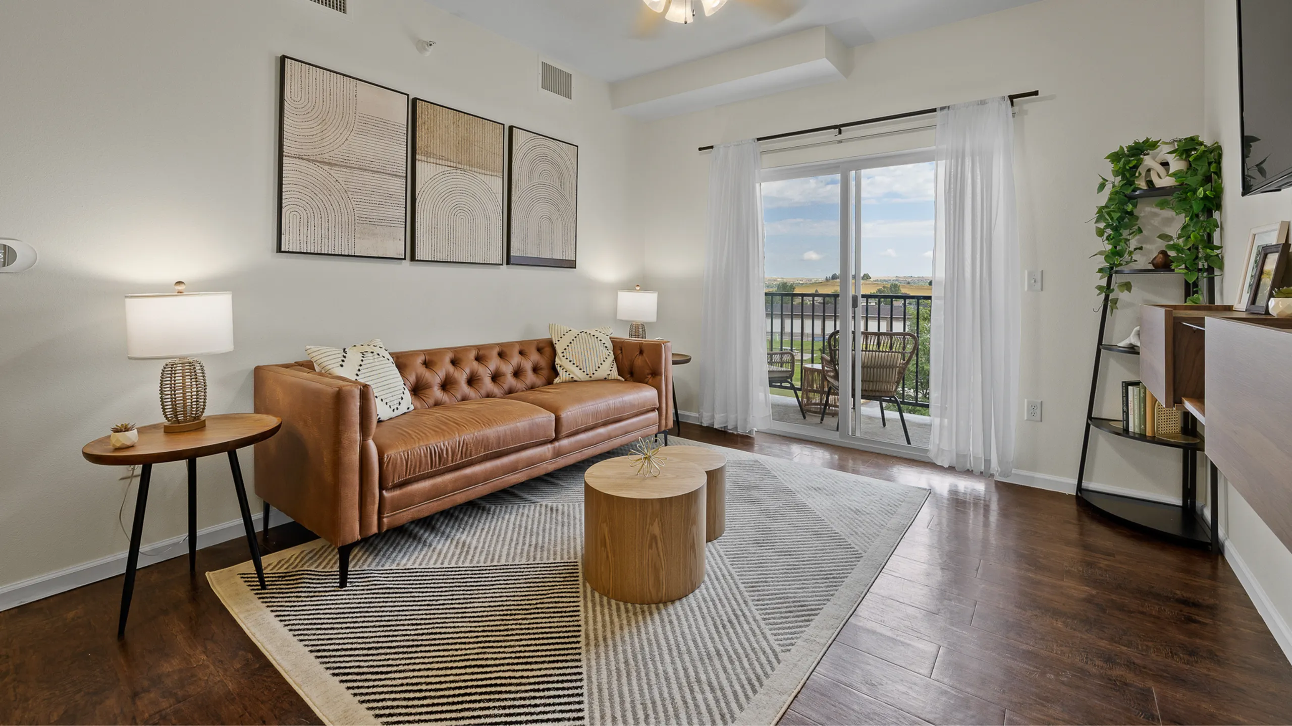 Inviting living room with modern decor, featuring a sleek leather couch, abstract wall art, and elegant wooden accents, opening to a scenic balcony with serene views.