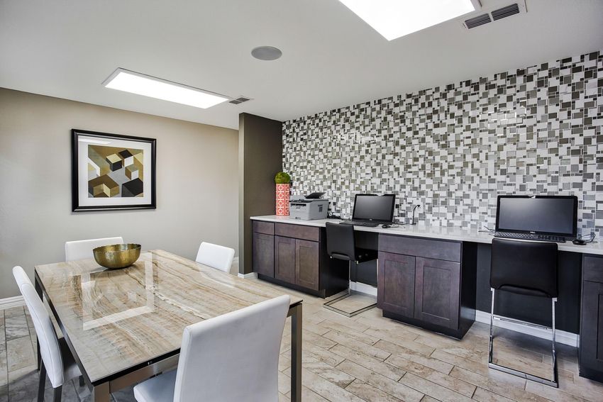 Modern office space featuring a stylish table with a decorative bowl, two sleek workstation desks with computers, and a geometric patterned accent wall. Bright lighting from skylights enhances the inviting atmosphere.