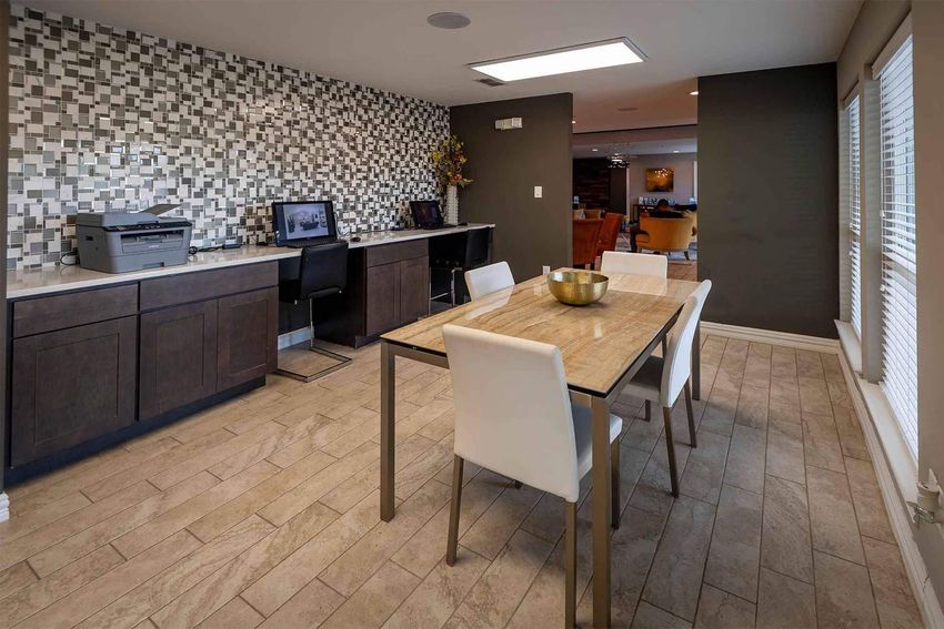 A modern, open-concept kitchen and dining area featuring a stylish dining table surrounded by white chairs, a dark wood cabinet, a printer station, and a decorative wall with mosaic tiles. Natural light streams in through windows, creating a warm and inviting atmosphere.