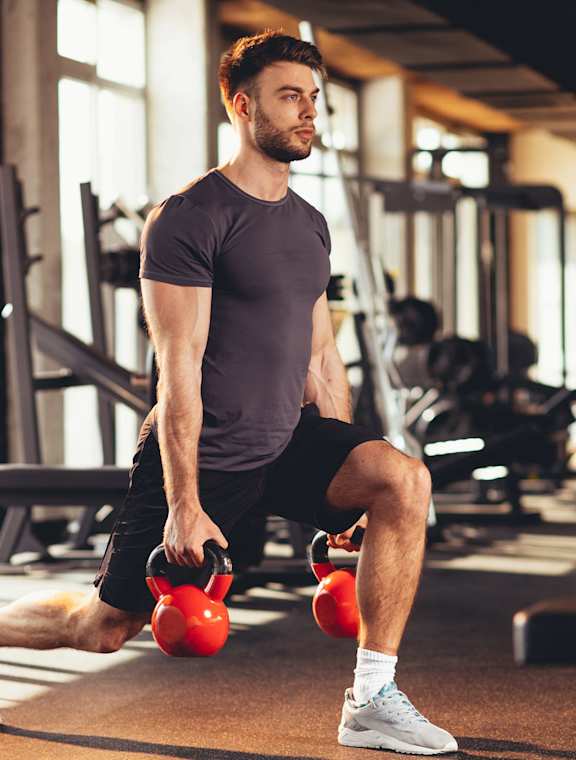 A man in a gym doing a kettlebell lunge.