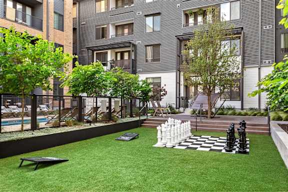 A chess set sits on a green lawn in front of a building.